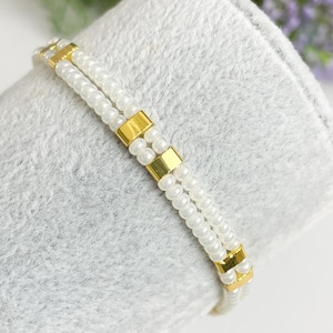 May include: A white beaded bracelet with gold square beads.