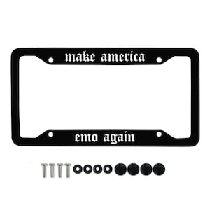 May include: Black license plate frame with the text "make america" above and "emo again" below in white gothic font. Includes mounting hardware: screws, washers, and black screw caps. The frame is rectangular with rounded corners.