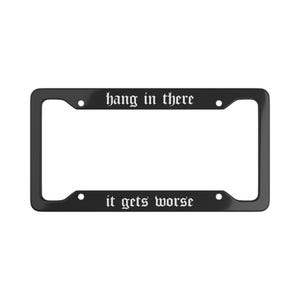 May include: Black license plate frame with the phrases "hang in there" and "it gets worse" in white gothic font. The frame has a rectangular shape with rounded corners and mounting holes.