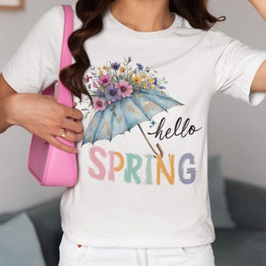 Puede incluir: Camiseta blanca con un diseño floral colorido y una sombrilla. El texto "hello spring" está escrito en letras de colores.