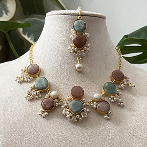May include: A gold necklace with green and pink stones and white pearls. Matching earrings with green and pink stones and white pearls.