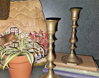 May include: Two antique brass candle holders with a hexagonal base. The candle holders are on top of a stack of books.