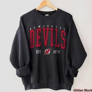 May include: Black sweatshirt with the words "New Jersey Devils" in red and white lettering. The logo of the New Jersey Devils hockey team is below the text with the words "Est. 1974".