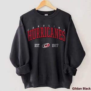 May include: Black sweatshirt with a red and white Carolina Hurricanes logo and the text "Carolina Hurricanes Est. 1997".