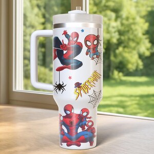 May include: A white insulated tumbler featuring various Spider-Man illustrations in red, blue, and black. The tumbler has a white handle, a silver rim, and a white lid. The words "Spider-Man" are printed on the side.