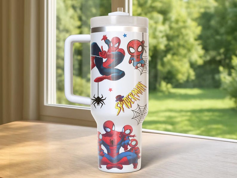 May include: A white insulated tumbler featuring various Spider-Man illustrations in red, blue, and black. The tumbler has a white handle, a silver rim, and a white lid. The words "Spider-Man" are printed on the side.