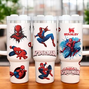 Op de afbeelding: Drie witte ge&iuml;soleerde mokken met handvatten, met Spider-Man graphics. De mokken hebben een wit deksel en een doorzichtig rietje. E&eacute;n mok heeft het Stanley-logo. De Spider-Man ontwerpen bevatten verschillende actieposes en de logo's "Spider-Man" en "Ultimate Spider-Man".