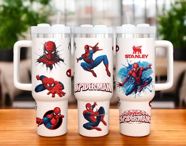 Op de afbeelding: Drie witte ge&iuml;soleerde mokken met handvatten, met Spider-Man graphics. De mokken hebben een wit deksel en een doorzichtig rietje. E&eacute;n mok heeft het Stanley-logo. De Spider-Man ontwerpen bevatten verschillende actieposes en de logo's "Spider-Man" en "Ultimate Spider-Man".