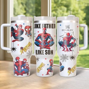 May include: Three white insulated tumblers with handles, featuring Spider-Man graphics. One tumbler has the text "LIKE FATHER LIKE SON". Each tumbler has a white lid and a straw. The brand name "STANLEY" is visible on one tumbler.