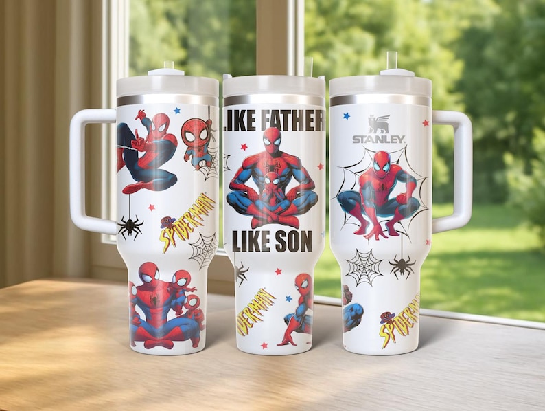 May include: Three white insulated tumblers with handles, featuring Spider-Man graphics. One tumbler has the text "LIKE FATHER LIKE SON". Each tumbler has a white lid and a straw. The brand name "STANLEY" is visible on one tumbler.