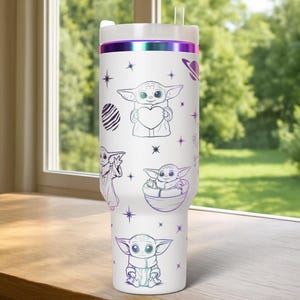 May include: White tumbler with a lid and straw, featuring illustrations of a character holding a heart, in a pod, and other poses. The design includes stars and a planet. The top rim has a purple and green iridescent band.