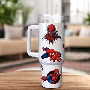 Op de afbeelding: Een witte beker met een handvat en een rietje, versierd met rode en blauwe Spider-Man afbeeldingen. De beker heeft een wit deksel en een grote handgreep. Het ontwerp toont verschillende actieposes van de superheld.