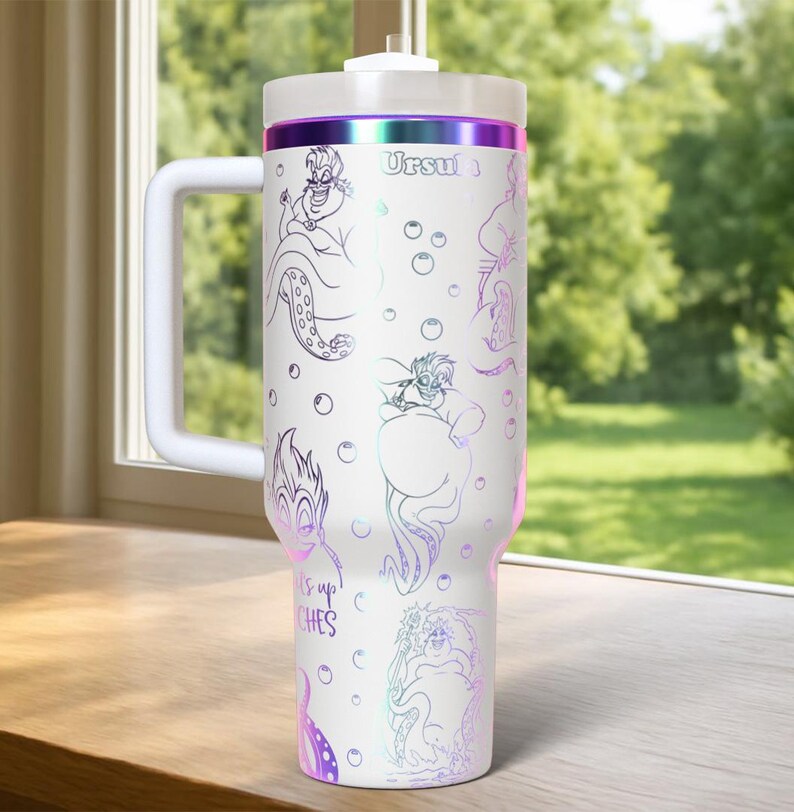 Może przedstawiać: Biały kubek termiczny z uchwytem, z Urszulą z Małej Syrenki. Projekt zawiera ilustracje liniowe Urszuli i tekst "It's up to witches". Kubek ma białą pokrywę i fioletowy, opalizujący pasek.