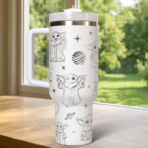 May include: White insulated tumbler with a handle, featuring a repeating pattern of a cartoon character in various poses, along with stars and planets. The tumbler has a white lid and handle, and a silver band near the top.