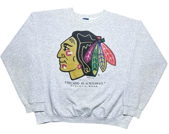 May include: A light gray sweatshirt featuring the Chicago Blackhawks logo. The logo depicts a Native American profile in yellow, black, and red, with the text "CHICAGO BLACKHAWKS ATHLETIC WEAR" below.