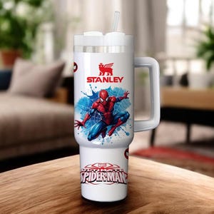 Op de afbeelding: Witte Stanley-beker met een Spider-Man-afbeelding. De beker heeft een handvat, een wit deksel en een rietje. De Spider-Man-afbeelding toont de superheld in een dynamische pose met blauwe en rode kleuren. De beker heeft ook de tekst "ULTIMATE SPIDER-MAN".