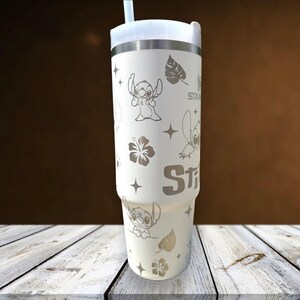 Może przedstawiać: Biały kubek ze srebrną obręczą i pokrywką, z wytrawionymi wzorami postaci Stitcha, gwiazd i tropikalnych kwiat&oacute;w. Kubek zawiera białą słomkę i jest przeznaczony do zimnych napoj&oacute;w.