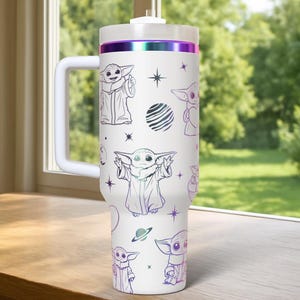 May include: White travel mug featuring illustrations of a character in a robe, with a handle and a lid. The mug has a purple and iridescent band around the top. The design includes stars and planets.