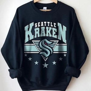 K&ouml;nnte beinhalten: Schwarzes Sweatshirt mit einem blau-wei&szlig;en Seattle Kraken Logo und dem Schriftzug "Seattle Kraken" in Wei&szlig;.
