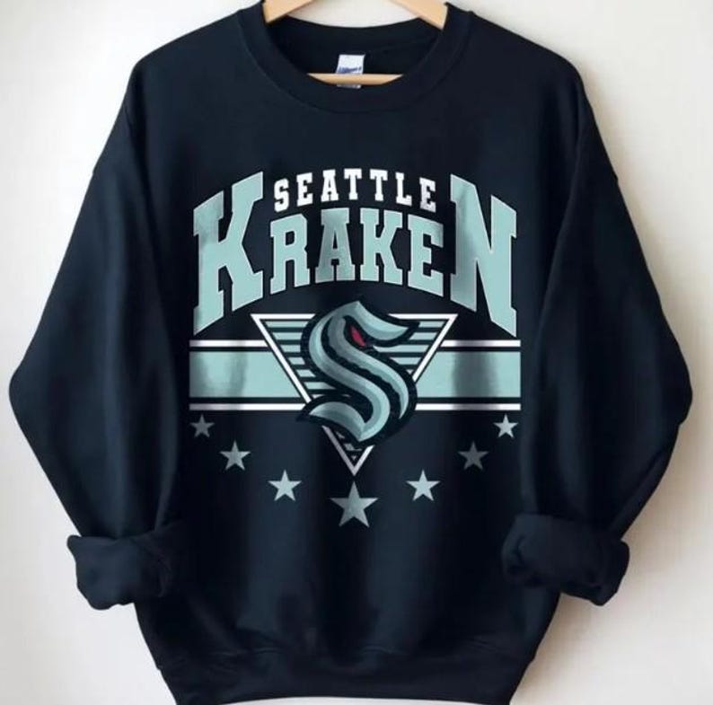 K&ouml;nnte beinhalten: Schwarzes Sweatshirt mit einem blau-wei&szlig;en Seattle Kraken Logo und dem Schriftzug "Seattle Kraken" in Wei&szlig;.