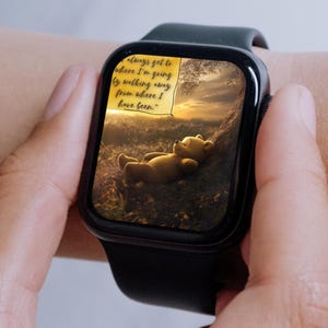 May include: A black smartwatch displaying an illustration of Winnie the Pooh on the screen. The illustration shows Winnie the Pooh lying on his back, with a sunset in the background. A yellow sticky note with handwritten text is visible on the screen: "always get to where I'm going by walking away from where I have been."
