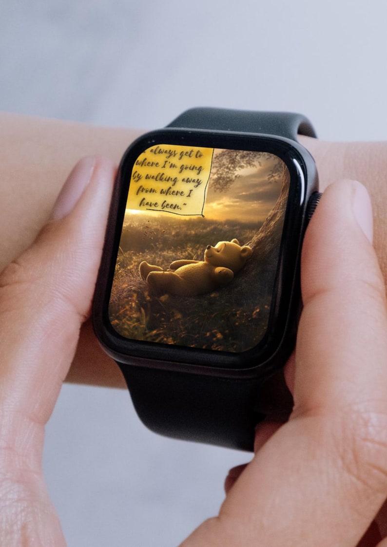 May include: A black smartwatch displaying an illustration of Winnie the Pooh on the screen. The illustration shows Winnie the Pooh lying on his back, with a sunset in the background. A yellow sticky note with handwritten text is visible on the screen: "always get to where I'm going by walking away from where I have been."
