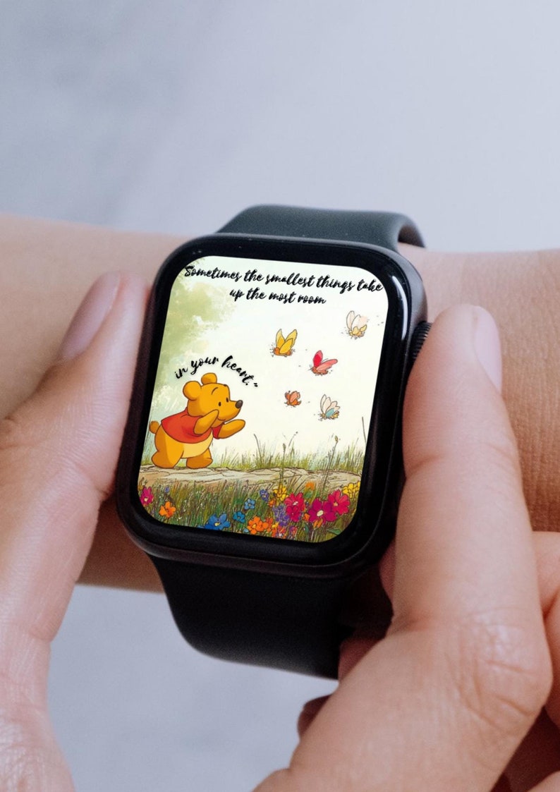 May include: A black smartwatch with a Winnie the Pooh themed watch face. The watch face features a cartoon image of Winnie the Pooh with the quote "Sometimes the smallest things take up the most room in your heart."  The background is a watercolour style illustration of a meadow with butterflies.