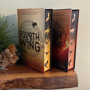 Puede incluir: Dos novelas de fantas&iacute;a con cubiertas doradas y rojas. Las cubiertas presentan dragones y los t&iacute;tulos "Cuarta Ala" y "Llama de Hierro".