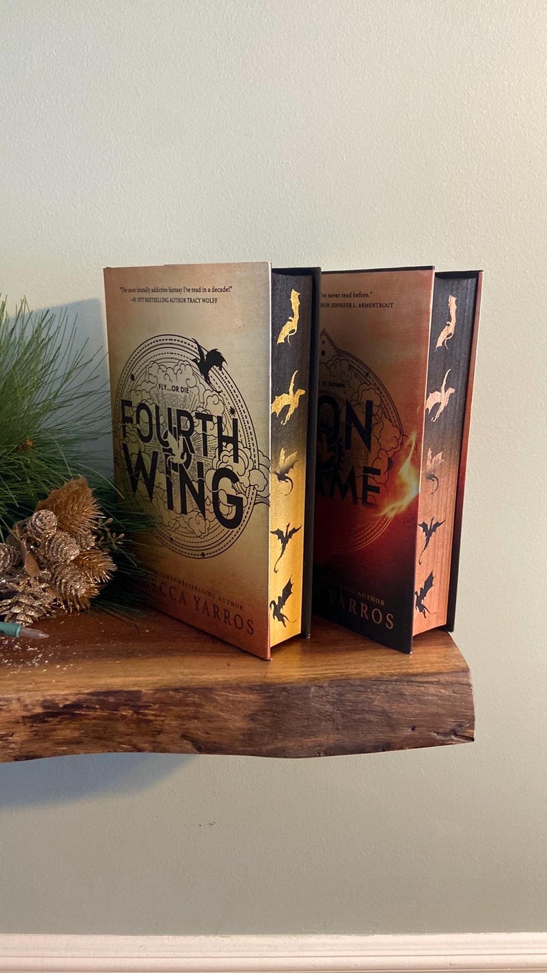 Puede incluir: Dos novelas de fantas&iacute;a con cubiertas doradas y rojas. Las cubiertas presentan dragones y los t&iacute;tulos "Cuarta Ala" y "Llama de Hierro".