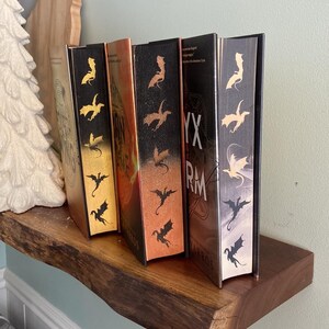 Puede incluir: Cuatro libros de tapa dura con cubiertas negras y dise&ntilde;os de dragones dorados, cobre y plata en las espinas. Los libros se titulan "The Inheritance Cycle" y "Eragon".