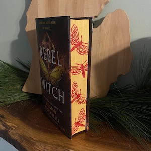 May include: A book titled "Rebel Witch" with a yellow and red butterfly design on the spine. The book is part of a series and is book two. The author is Kristen Ciccarelli.