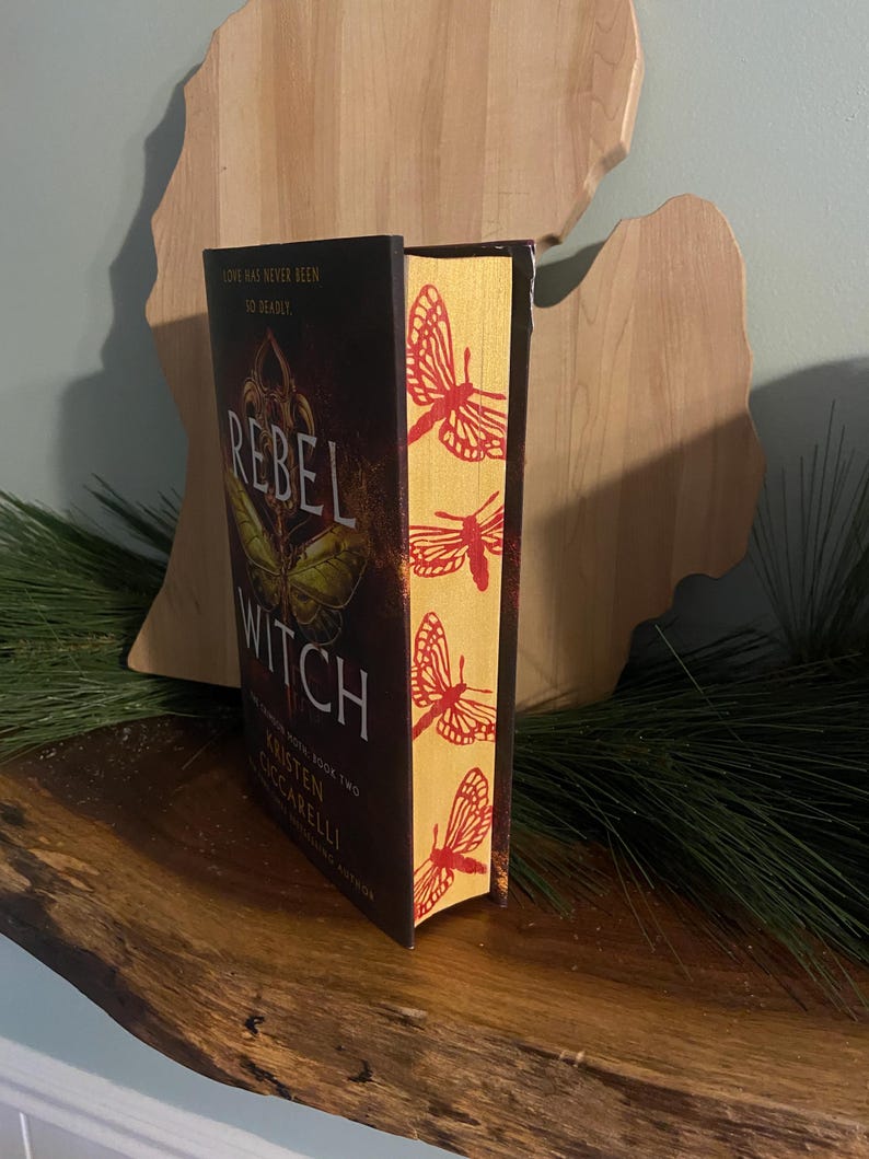 May include: A book titled "Rebel Witch" with a yellow and red butterfly design on the spine. The book is part of a series and is book two. The author is Kristen Ciccarelli.
