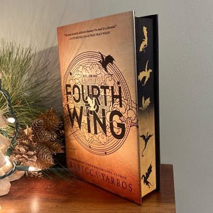 Puede incluir: Un libro titulado "Fourth Wing" de Rebecca Yarros. La portada presenta una silueta de drag&oacute;n y las palabras "Fly or Die". El lomo es negro con siluetas de dragones doradas.
