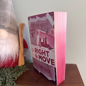 May include: A paperback book titled The Right Move by Liz Tomforde with a pink-tinted cover featuring a city skyline graphic, a basketball hoop, and pink floral accents. The book has bright pink sprayed edges on the pages and a white spine.
