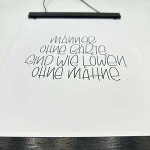 Puede incluir: Una impresión enmarcada en negro con el texto "Männer ohne Bärte sind wie Löwen ohne Mähne" en blanco.