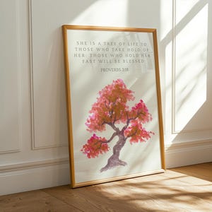 Könnte beinhalten: Ein gerahmter Druck mit einem Aquarellbild eines rosa und orangefarbenen Baumes. Der Text "SHE IS A TREE OF LIFE TO THOSE WHO TAKE HOLD OF HER: THOSE WHO HOLD HER FAST WILL BE BLESSED PROVERBS 3:18" ist unter dem Baum gedruckt.