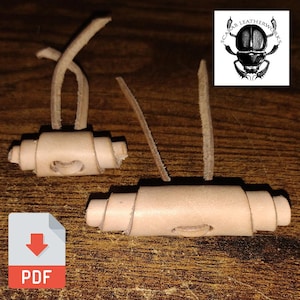Puede incluir: Dos cierres de palanca de cuero natural con correas de cuero en bucle. Los cierres son cilíndricos con un agujero ovalado central. Un icono PDF está en la esquina inferior izquierda y un logotipo de escarabajo en la esquina superior derecha.