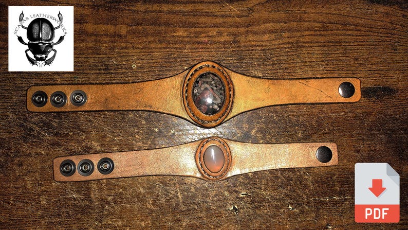 May include: Two leather bracelets with metal snaps and a round stone inlay. The top bracelet has a brown stone inlay and the bottom bracelet has a pink stone inlay.