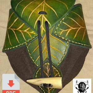 Puede incluir: Una bolsa de cuero verde y marrón con un diseño de hojas. La bolsa tiene un cierre de cordón y un botón de madera. La bolsa está hecha a mano y tiene un aspecto rústico.