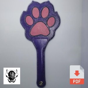 May include: Purple leather paddle with a pink paw print design. The paddle has a stitched edge and a loop at the end of the handle.