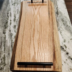 May include: A wooden serving tray with a natural wood finish and two black metal handles. The tray has a live edge design and is perfect for serving food or drinks.