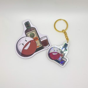 Puede incluir: Dos pegatinas y un llavero con un personaje de dibujos animados con un diseño rojo y blanco, una botella de licor y un vaso de chupito. El llavero tiene un anillo y una cadena dorados.
