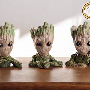 Puede incluir: Tres macetas inspiradas en Groot. Cada maceta presenta un diseño detallado y texturizado con una base marrón claro y detalles verdes. Las macetas tienen ojos grandes y oscuros y una expresión sonriente, perfectas para plantas pequeñas.
