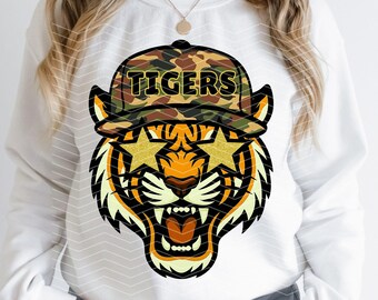 May include: White sweatshirt featuring a tiger graphic with star-shaped sunglasses and a camouflage hat that reads "TIGERS". The tiger has orange, black, and yellow details, with an open mouth showing teeth.