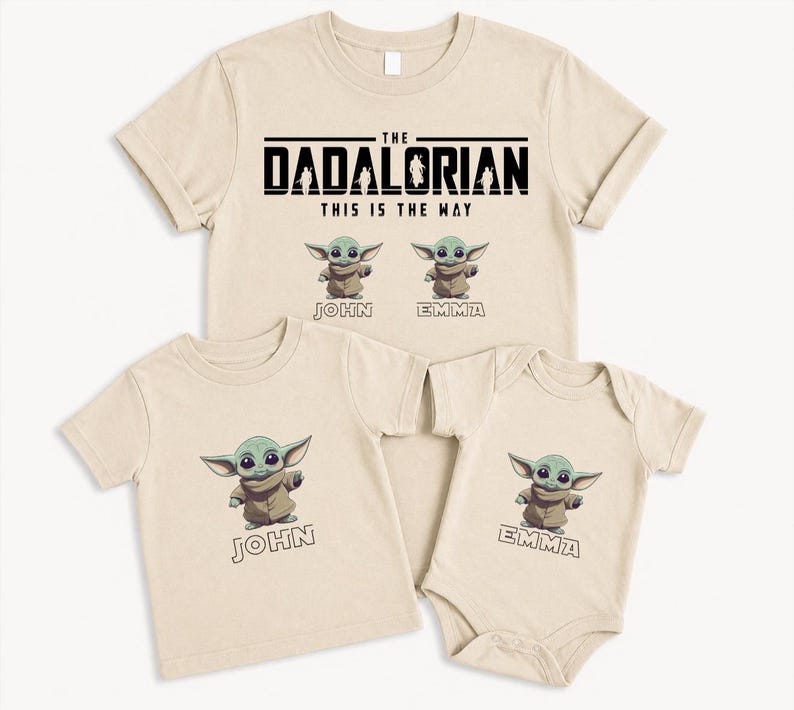 K&ouml;nnte beinhalten: Beige T-Shirts und ein Body mit einer Cartoonfigur. Das Erwachsenen-Shirt tr&auml;gt die Aufschrift "The Dadalorian" mit "This is the Way" darunter. Die Kinderhemden haben das Bild der Figur und die Namen "John" und "Emma".