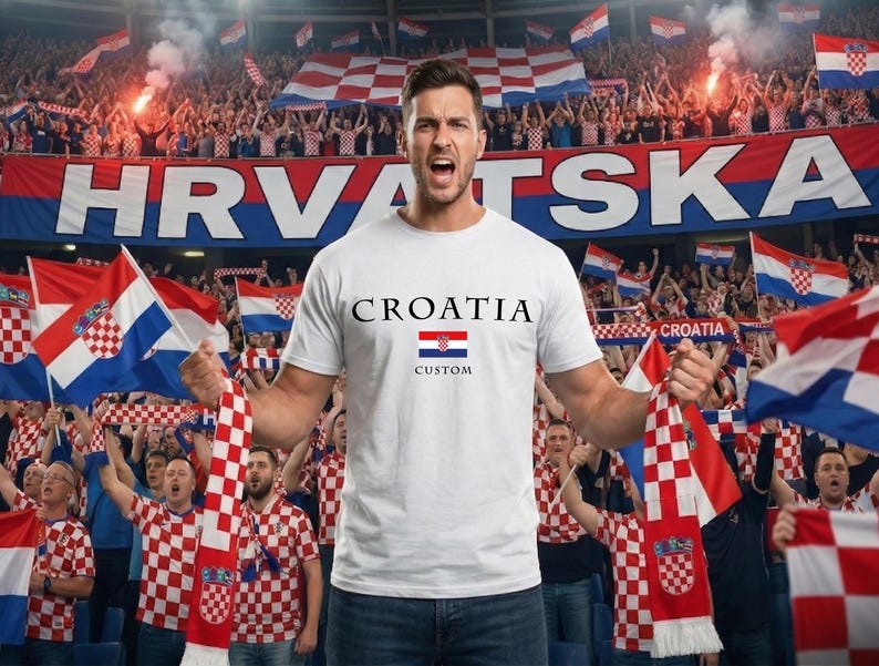 May include: A white t-shirt with "CROATIA" printed in black, a Croatian flag graphic, and the word "CUSTOM" in black. The image shows a person holding a Croatian flag and scarf in a stadium filled with fans.
