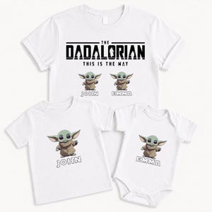 K&ouml;nnte beinhalten: Wei&szlig;e T-Shirts und ein Body mit einer gr&uuml;nen Alien-Figur in einem braunen Umhang. Die Shirts tragen den Text "THE DADALORIAN THIS IS THE WAY" und die Namen "JOHN" und "EMMA".