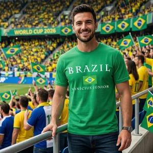 Może przedstawiać: Mężczyzna w zielonej koszulce z białym napisem "BRAZIL", brazylijską flagą i nazwiskiem "Vin&iacute;cius J&uacute;nior". W tle stadion z kibicami trzymającymi brazylijskie flagi i napisem "WORLD CUP 2026".
