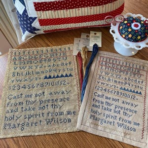 May include: Two rectangular linen samplers featuring cross-stitched alphabets, numbers, and the text 'Cast me not away from thy presence and take not thy holy spirit from me Margaret Wilson'. Includes embroidery floss, a pincushion, and a quilt.