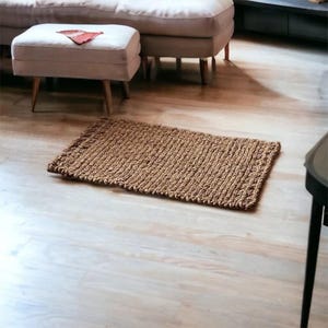 May include: A brown woven rug with a textured surface. The rug is placed on a light wood floor.